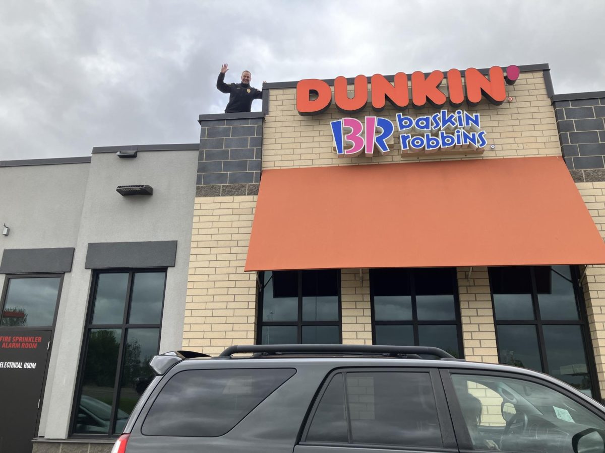 Woodbury police commander Tom Ehrenberg waves from atop the restaurant for today's Cop on a Roof.