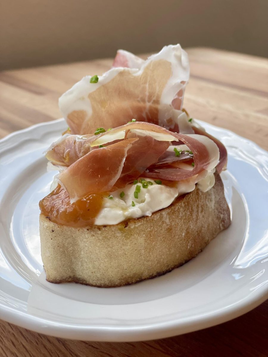 Prosciutto bruschetta topped with creamy stracciatella, melon marmalade, and fresh chives on toasted bread.