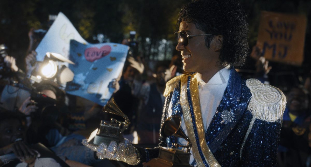 A man stands in front of a crowd, holding awards