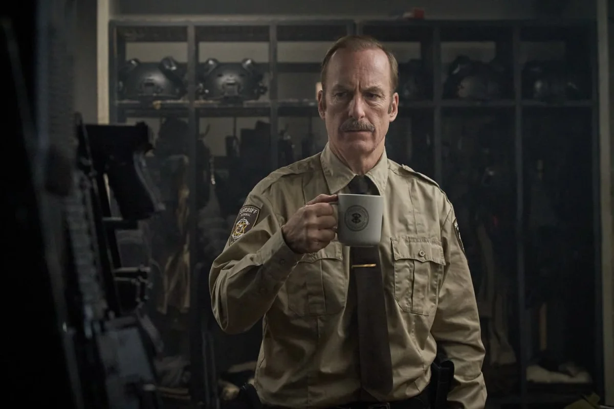 A police officer stands in a weapons armory holding a cup of coffee