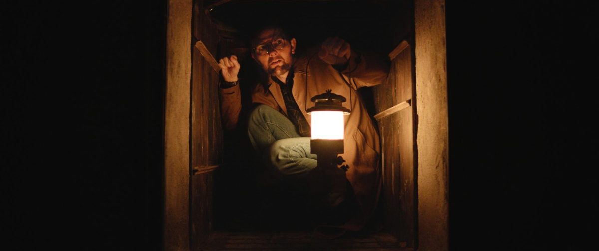 A man holds a lantern surrounded by darkness